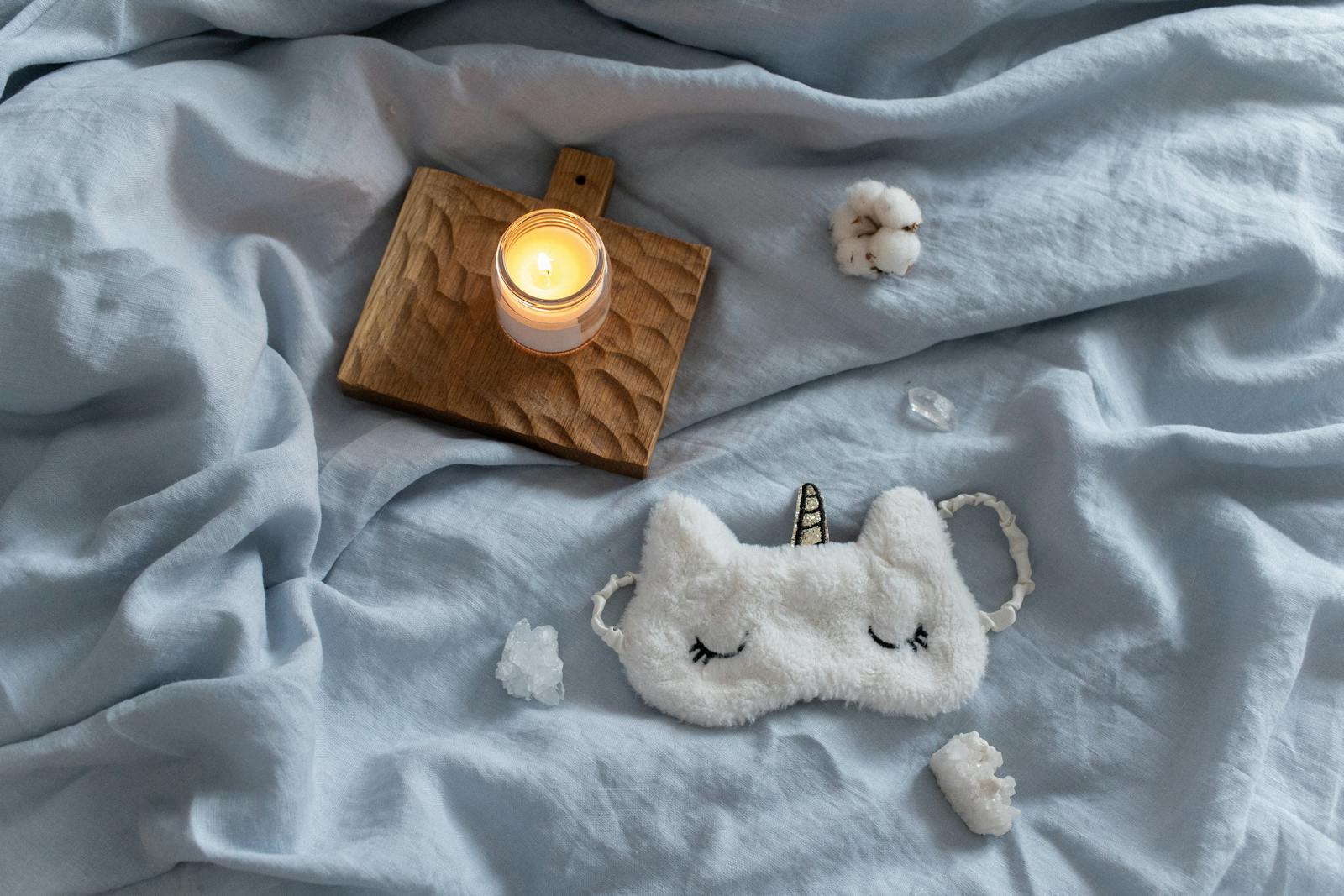 Calming sleep mask and candle on soft bedding